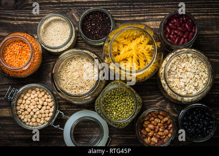 Getreide, Hülsenfrüchte und Bohnen in Gläsern auf dunklen Holztisch. Stockfoto