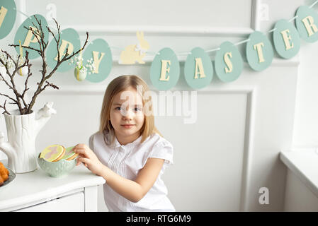 Niedliches kleinkind Mädchen in einem weißen T-Shirt ist Essen mit Ostereier am Ostersonntag. Stockfoto
