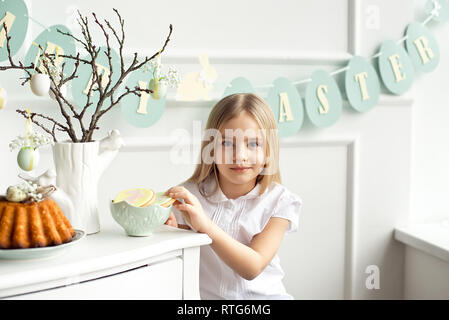 Niedliches kleinkind Mädchen in einem weißen T-Shirt ist Essen mit Ostereier am Ostersonntag. Stockfoto
