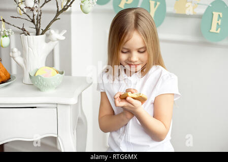 Niedliches kleinkind Mädchen in einem weißen T-Shirt ist Essen mit Ostereier am Ostersonntag. Stockfoto