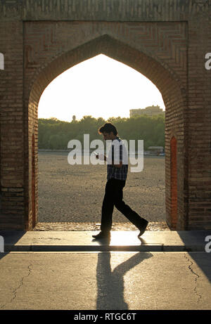 Isfahan, Iran - Juni 14, 2018: Ein Mann geht auf den berühmten Khaju Brücke in den Abendstunden, während sein Smartphone prüfen. Stockfoto