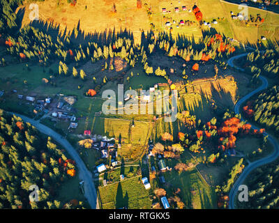 Gebogene Serpentinenstraße trog Herbst Wald und das Dorf. High Mountain Pass in den Karpaten, in der Ukraine. Herbst Startseite Luftbild von Drone. Stockfoto