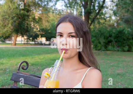 Junge hübsche Mädchen trinkt Limonade aus der Flasche durch den Stroh mit eine große Freude. Stockfoto