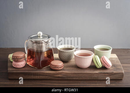 Verschiedene Arten von Makronen mit Glas Teekanne und Tassen auf grauen Hintergrund closeup Stockfoto