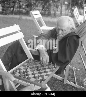 Schachspieler in den 1950er Jahren. Ein älterer Mann in einem gemütlichen Garten Stuhl ist Schach spielen mit jemand, und macht eine Bewegung auf dem Schachbrett. Foto Kristoffersson Ref 21-9. Schweden 1952 Stockfoto