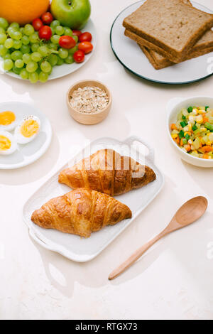 Gesundes Frühstück serviert mit Milch, Croissants, Eier, Cerealien, Müsli und Obst. Stockfoto