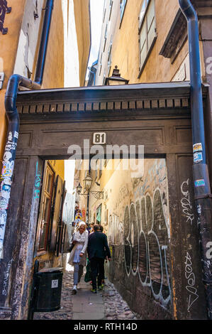 Stockholm, Schweden, 26. Mai 2017: Super engen mittelalterlichen Straße mit Holz- arch Eingangstor, wandern Leute, schäbige geknackt gelb orange Stuck bui Stockfoto