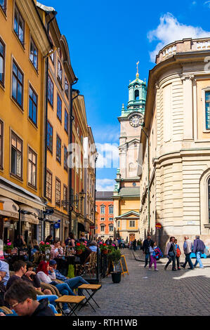 Stockholm, Schweden, 26. Mai 2017: Gemütliche mittelalterliche Straße mit dem gehen Menschen, Unternehmen, gelb orange Gebäude, Fassaden und Storkyrkan tower i Stockfoto