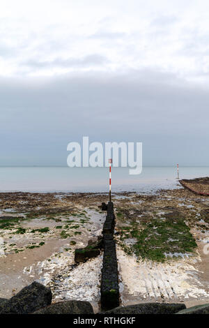 Konkrete Wave Breaker mit Navigation Pol am Ende, ragt heraus auf die Gezeiten Regal von Kreide und Sand, der am Ufer des Meeres, Margate. Düster bedeckt grauer Himmel. Stockfoto