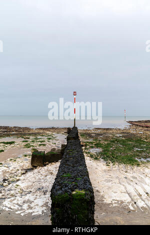 Konkrete Wave Breaker mit Navigation Pol am Ende, ragt heraus auf die Gezeiten Regal von Kreide und Sand, der am Ufer des Meeres, Margate. Düster bedeckt grauer Himmel. Stockfoto