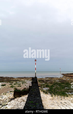 Konkrete Wave Breaker mit Navigation Pol am Ende, ragt heraus auf die Gezeiten Regal von Kreide und Sand, der am Ufer des Meeres, Margate. Düster bedeckt grauer Himmel. Stockfoto