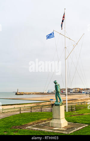 Bronzestatue des Rettungsbootes Mann am Nayland Rock auf Margate Seafront. Fahnenmast flying Union Jack und die griechische Flagge. Margate Strand und Hafen hinter Stockfoto