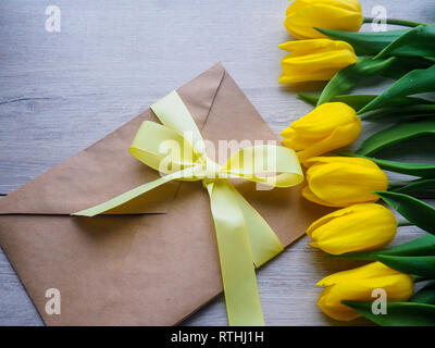 Strauß gelber Tulpen auf Holz- Hintergrund mit Umschlag, mit einem Band Platz für Text gebunden. Stockfoto