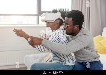 Stattlichen Paare mit elektronischen Geräten futuristische Technologie. Afrikanische Frau spielen atemberaubende computer spiel mit VR-Headset und ihrem Ehemann er Stockfoto