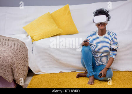 Happy and african american Studentin in Blau abgestreift t-shirt erhalten Sie über VR-Headset Gläser der virtuellen Realität erleben, sitzen auf den Yello Stockfoto