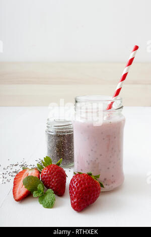 Glas frische Erdbeere Smoothie oder Milchshake mit ausgefallenen rot-weiß Stroh, kleines Glas von Chia Samen, verziert mit ein paar echten Erdbeeren und Minze er Stockfoto