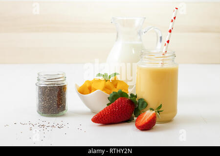 Glas frische Mango Smoothie oder Mango Milchshake mit Milch in Glas Krug, Mangostückchen in Porzellan Schüssel und nur wenige echte frische Erdbeeren auf whit Stockfoto