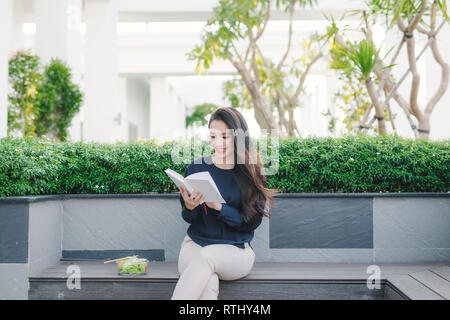 Glückliche junge Frau im Park auf sonnigen Sommertag Buch zu lesen. Fröhliches schönes Mädchen auf den schönen Tag. Stockfoto