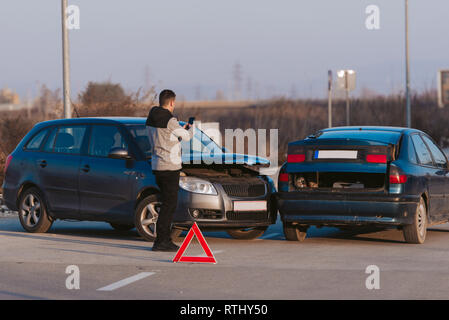 Ein Mann mit einem Smart Phone ein Foto von den Schaden an seinem Auto durch einen Autounfall verursacht zu nehmen Stockfoto