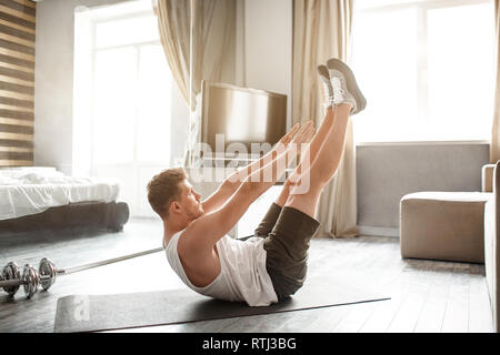 Die Jungen gut gebauten Mann gehen in für den Sport in der Wohnung. Er lag auf dem Rücken und Füße mit den Händen erreichen. Junger Mann ausdehnen. Yoga Übung Stockfoto