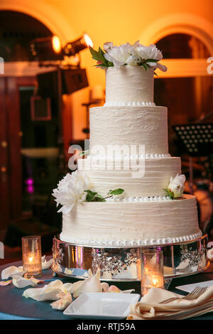 Mehrstufige Hochzeitstorte mit weißen Blumen und Sahne frosting auf einem Tisch mit Kerzen - Hochzeitstorte Serie Stockfoto