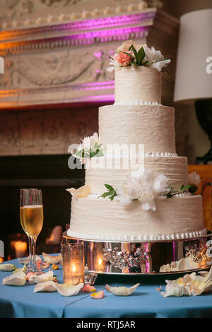 Mehrstufige Hochzeitstorte mit weißen Blumen und Sahne frosting auf einem Tisch mit Kerzen und Champagner Gläser - Hochzeitstorte Serie Stockfoto