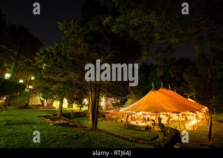 Eine Hochzeit Zelt in der Nacht von Bäumen mit einem orangefarbenen Leuchten von den Lichtern umgeben. - Hochzeit Zelt Serie Stockfoto