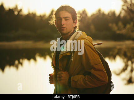 Seitenansicht eines Reisenden tragen Rucksack stand neben einem See. Junger Mann, der in der Nähe von einem See auf eine Erforschung Reise. Stockfoto