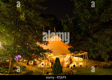 Eine Hochzeit Zelt in der Nacht von Bäumen mit einem orangefarbenen Leuchten von den Lichtern umgeben. - Hochzeit Zelt Serie Stockfoto