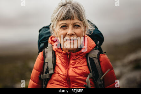 Nahaufnahme von einer älteren Frau in Jacke und einen Rucksack. Ältere Frau auf einer Wanderung an einem Wintertag. Stockfoto