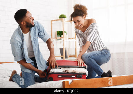 Afrikanisch-amerikanisches Paar versuchen, Koffer auf das Bett zu schließen. Stockfoto