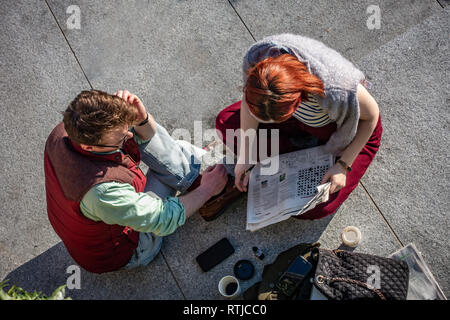 Junges Paar gesehen von oben den Austausch von Informationen über Ihre Kreuzworträtsel bei Kohle Tropfen Yard, Kings Cross, London, England Stockfoto