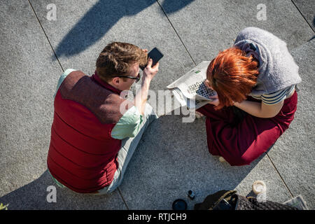 Junges Paar gesehen von oben den Austausch von Informationen über Ihre Kreuzworträtsel bei Kohle Tropfen Yard, Kings Cross, London, England Stockfoto