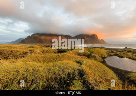 Zauberhafte Landschaft von Vestrahorn Berge und schwarzen Sand Dünen in Island bei Sonnenaufgang. Panoramablick auf die stokksnes Landspitze in einem bunten Seascape Stockfoto