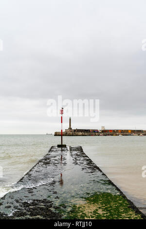 Margate Seafront. Algen bedeckt konkrete Wave Breaker mit Navigation Pol auf Ende, mit Hafen im Hintergrund. Bedeckt grauer Himmel. Ruhiges Meer. Stockfoto