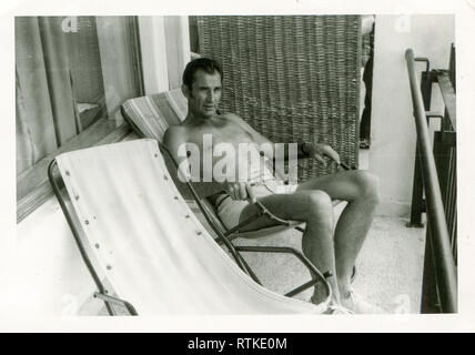 Amerika. Uns. 1940er. Ein Mann im Urlaub. Sitzt auf einem Stuhl auf dem Balkon des Hotels und Sunbathes. Stockfoto