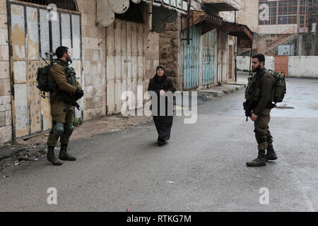 Eine palästinensische Frau durch israelische Soldaten Wache vor verschlossenen palästinensischen Geschäfte im Al-Shuhada Straße, dem zentralen Großhandelsmarkt des Hebron Region zu sein und wurde in den palästinensischen Kaufleuten nach Gewalt in der zweiten Intifada in der Altstadt von Hebron Westjordanland Israel geschlossen. Stockfoto