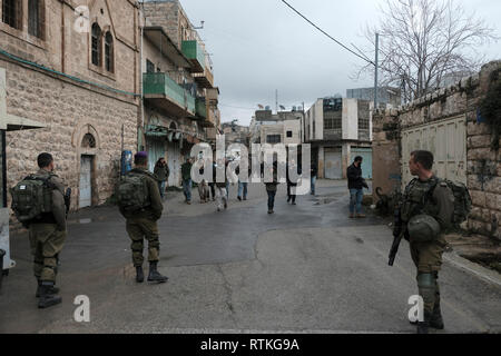 Israelische Soldaten escort eine Gruppe junger jüdischer Siedler durch versiegelte palästinensischen Geschäfte im Al-Shuhada Straße, dem zentralen Großhandelsmarkt des Hebron Region zu sein und wurde in den palästinensischen Kaufleuten nach Gewalt in der zweiten Intifada in der Altstadt von Hebron Westjordanland Israel geschlossen. Stockfoto