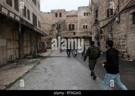 Israelische Soldaten escort eine Gruppe junger jüdischer Siedler durch versiegelte palästinensischen Geschäfte im Al-Shuhada Straße, dem zentralen Großhandelsmarkt des Hebron Region zu sein und wurde in den palästinensischen Kaufleuten nach Gewalt in der zweiten Intifada in der Altstadt von Hebron Westjordanland Israel geschlossen. Stockfoto