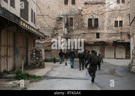 Israelische Soldaten escort eine Gruppe junger jüdischer Siedler durch versiegelte palästinensischen Geschäfte im Al-Shuhada Straße, dem zentralen Großhandelsmarkt des Hebron Region zu sein und wurde in den palästinensischen Kaufleuten nach Gewalt in der zweiten Intifada in der Altstadt von Hebron Westjordanland Israel geschlossen. Stockfoto