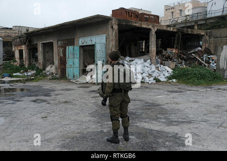 Israelischer Soldat steht Wache vor verlassenen palästinensischen Geschäften in der Nähe der Al-Shuhada Straße, die früher der zentrale Großmarkt der Region Hebron war und nach der Gewalt in der Zweiten Intifada in der Altstadt von Hebron im Westjordanland Israel für palästinensische Händler gesperrt wurde. Stockfoto