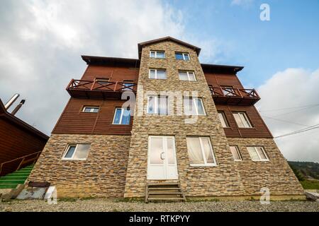 Fassade aus Holz neues Ferienhaus Haus der Materialien Holz und Stein mit dekorativen Balkon auf dem Hintergrund des blauen Himmels. Stockfoto