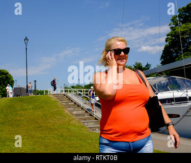 Eine Frau in leuchtend orange T-Shirt und Sonnenbrillen Uhren Aktivität an der Caledonian Canal Locks Spean Bridge schottischen Highlands Schottland Großbritannien Stockfoto