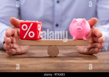 Die schützende Hand Balance zwischen Rot Prozentsatz kubische Block und Sparschwein auf hölzernen Wippe Stockfoto