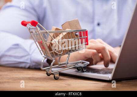 Nahaufnahme der Mann mit Laptop mit Miniatur Kartons In den Einkaufswagen Stockfoto