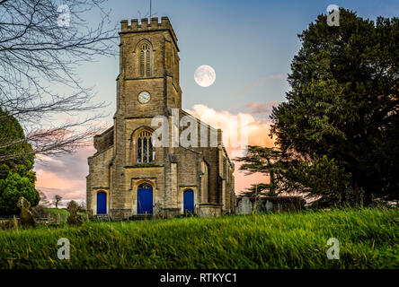 Mond im Himmel bei Sonnenuntergang hinter Kirche Clock Tower im Corsley, Wiltshire, UK am 20. Dezember 2015 Stockfoto