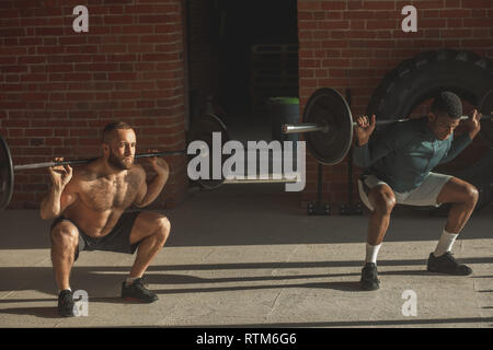 Sport, crossfit Lebensstil und Personen Konzept - Zwei entschlossen, im Kaukasus und in Afrika männliche Athleten mit Langhantel heben Gewicht bei Indoor Training gege Stockfoto