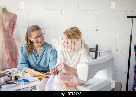 Zuversichtlich Näherin diskutieren Kleidung Skizze mit interessierten schöne weibliche Client, am Arbeitsplatz und auf Skizze sitzen Stockfoto