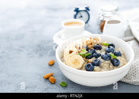 Haferbrei mit frischen Heidelbeeren, Bananen, Nüsse, Mandeln und Honig zum Frühstück Stockfoto