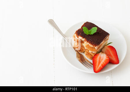 Tiramisu, hausgemachten süßen italienischen keine Backen dessert Käsekuchen, Schneiden von Kuchen auf kleine Teller mit frischer Minze und ein paar echte Erdbeeren verziert, auf wh Stockfoto